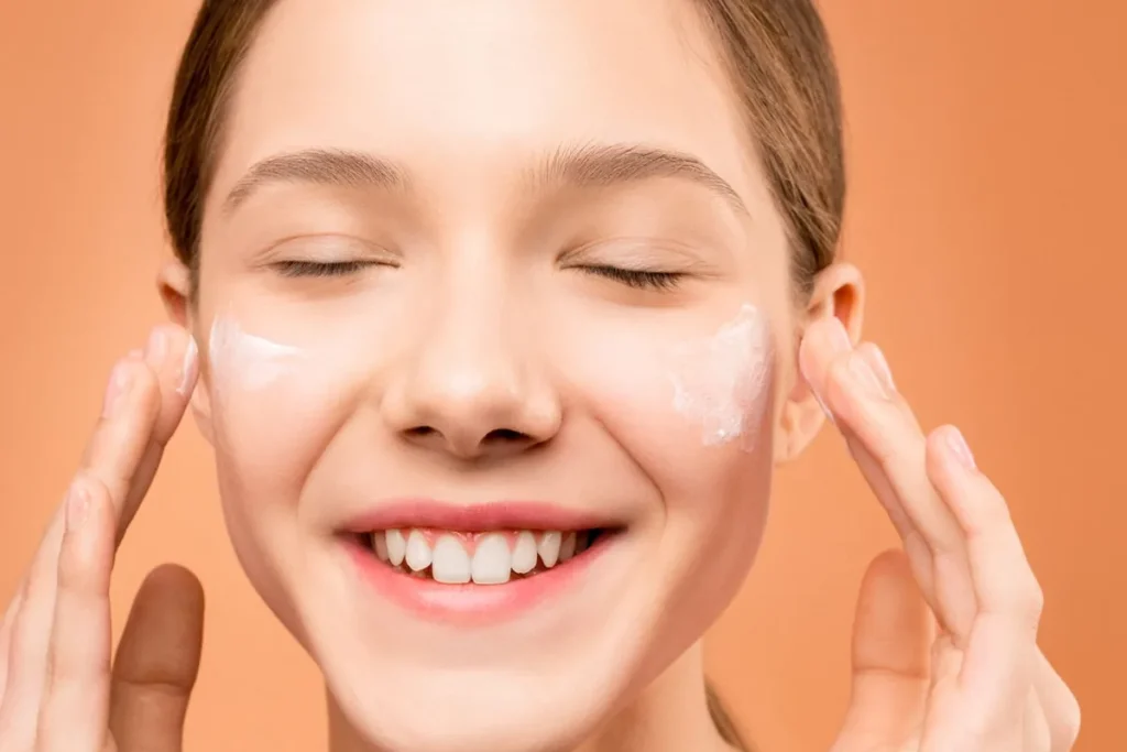 Người phụ nữ mỉm cười với má ửng hồng, mắt nhắm nghiền, trên nền màu cam.