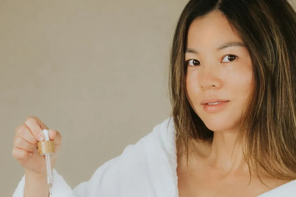 Người phụ nữ mặc áo choàng trắng cầm lọ serum có ống nhỏ giọt