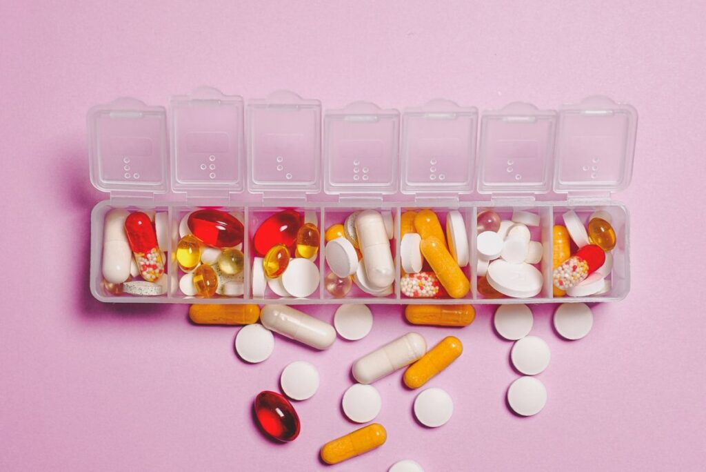 Weekly pill organiser filled with assorted vitamin capsules and tablets on a pink background