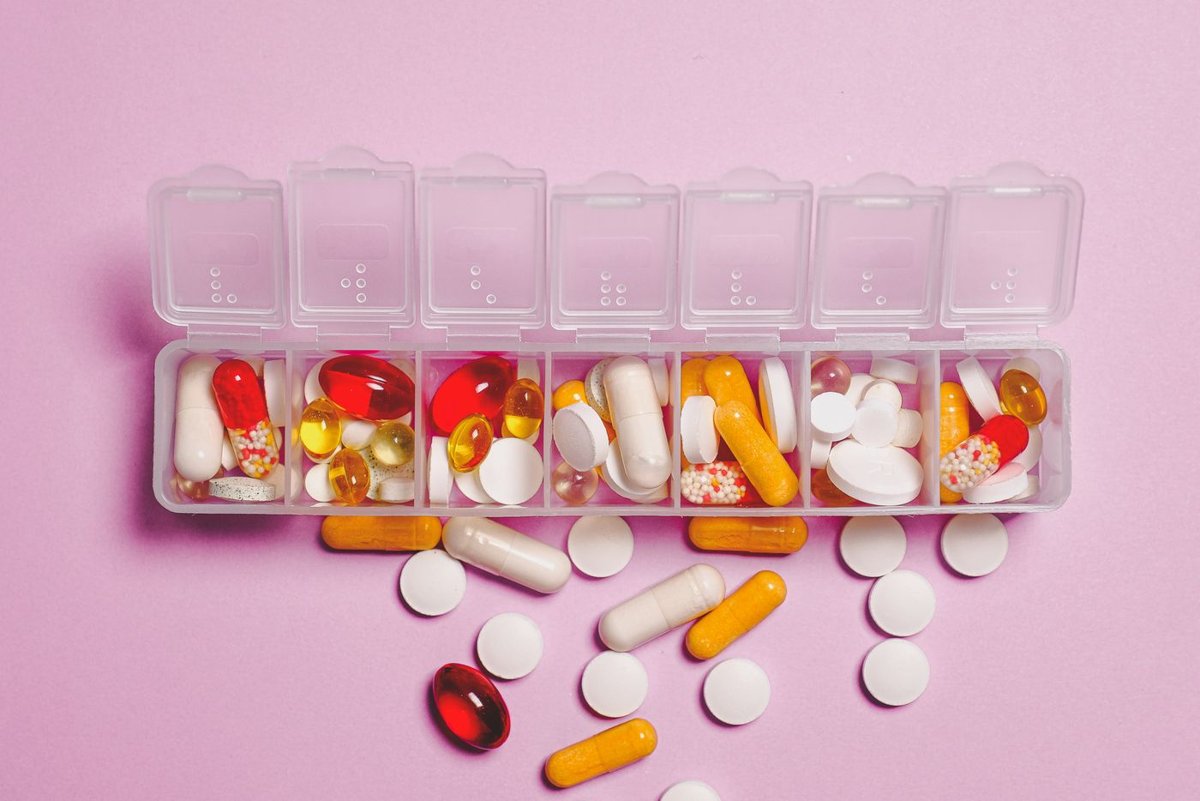 Weekly pill organiser filled with assorted vitamin capsules and tablets on a pink background