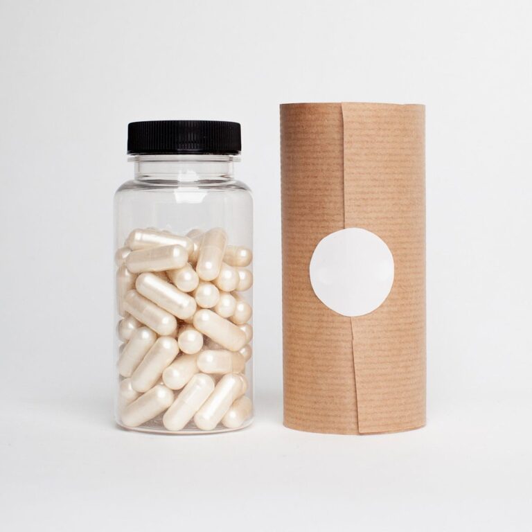 Clear bottle of white capsules beside a blank paper-wrapped label